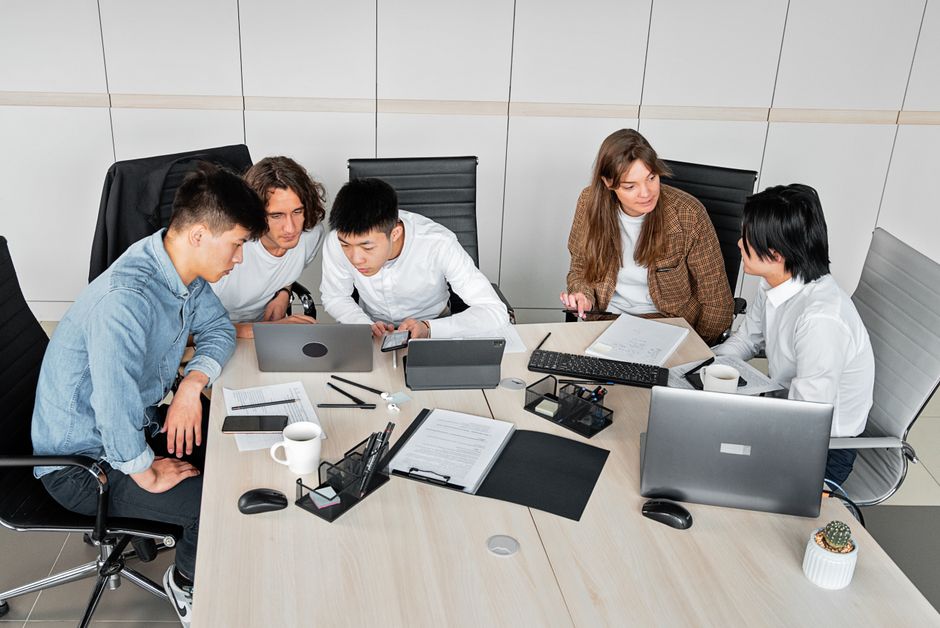 A diverse group of colleagues working together in an office setting with laptops and documents